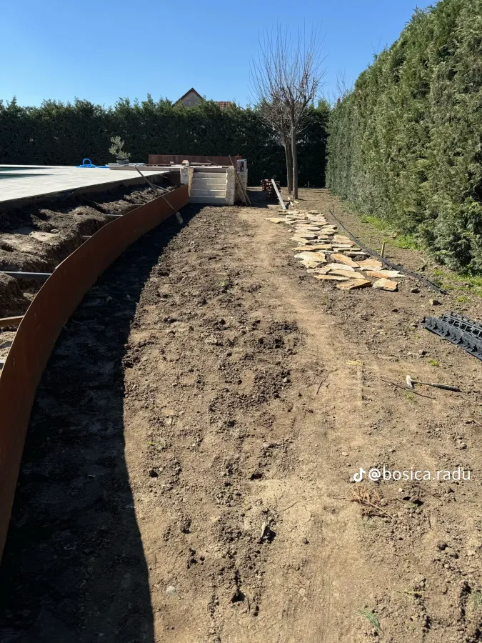 Bordura din oțel corten urmează linia curbată a piscinei, cu lespezi de piatră pregătite alături.